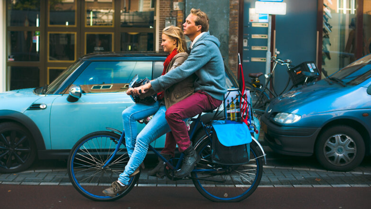 To personer kører på en cykel i en by, med varer bagpå, som symboliserer frihed og praktiske løsninger.